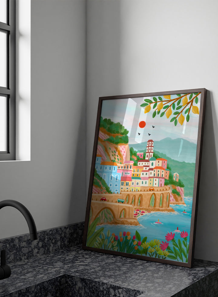 A colorful illustrated coastal town scene with pastel buildings, a stone bridge, blue water, mountains, flowers, and hanging yellow leaves. Shop Colorful Amalfi Coast by Nidhi Kachhadiya, a vibrant Italian coastal wall art print inspired by the Amalfi Coast, pastel villages, blue sea, and lemon trees.
