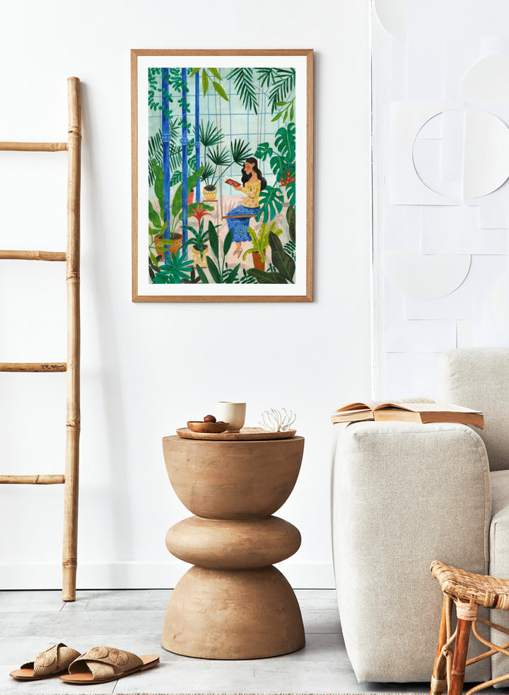 Woman sitting among plants in a room with bamboo and various greenery. Botanical Greenhouse Reader by Caroline Bonne Müller is a fine art print and wall poster featuring a woman reading in a lush indoor garden filled with tropical plants.