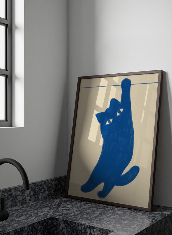 A stylized blue cat silhouette hanging from a thin horizontal line on a warm beige background. Hanging Blue Cat by The Art Concept is a playful cat art print featuring a blue cat dangling from one paw against a warm cream background.
