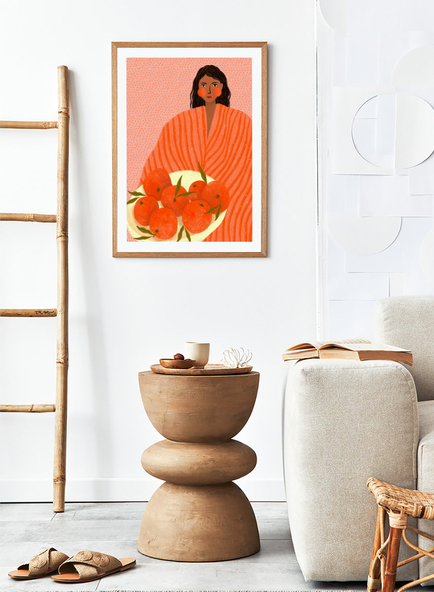 A stylized art print featuring a woman with dark hair wrapped in a bright orange striped blanket, holding a white plate of oranges against a pink dotted background. Woman Holding Oranges by Bea Müller colorful kitchen art print featuring a woman carrying fresh citrus fruit in warm orange and coral tones.