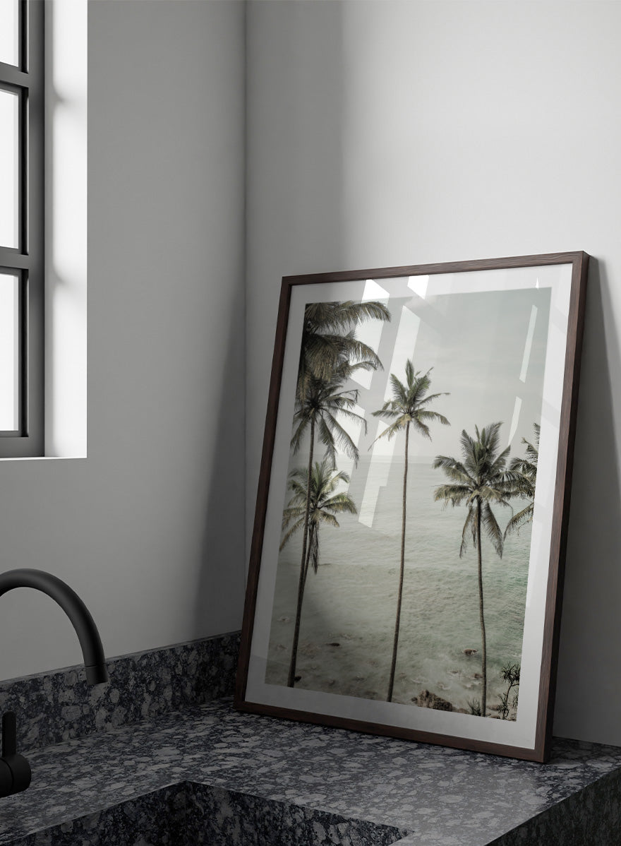 A framed photographic print of tropical coconut palm trees along a calm sea coastline. Tropical Dreams by Shot by Clint coastal photography print featuring tall palm trees, soft ocean waves, and muted tropical tones.