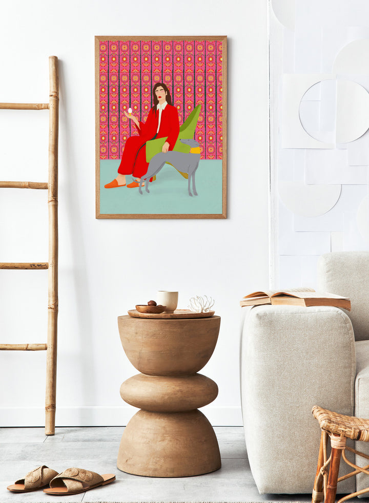 Woman in a red coat sitting on a green chair with a dog, against a pink patterned wall. Wonderful Egg by Jota de Jai is a whimsical modern art print of a woman in a red robe holding an egg with her greyhound, officially licensed wall poster with framing.