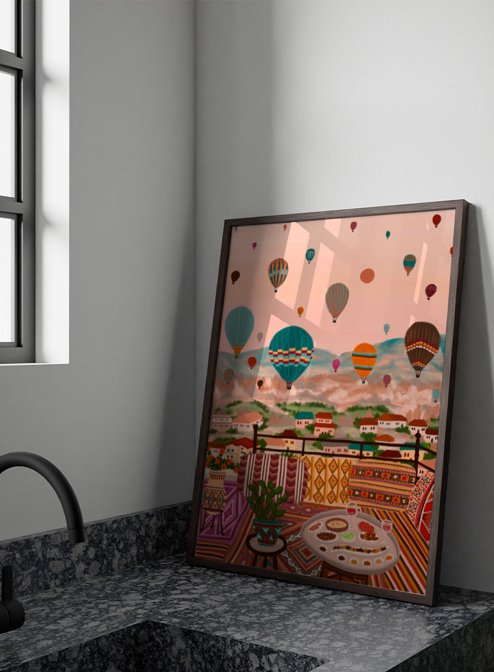A colorful art print depicting a scenic view of a hillside town with mountains in the background, filled with hot air balloons. In the foreground, a patterned outdoor seating area features a table with food and a potted plant. Shop Balloons Over Rooftop Dinner by Nidhi Kachhadiya, a colorful travel wall art print featuring hot air balloons, rooftop dining, patterned textiles, and teal and coral tones.