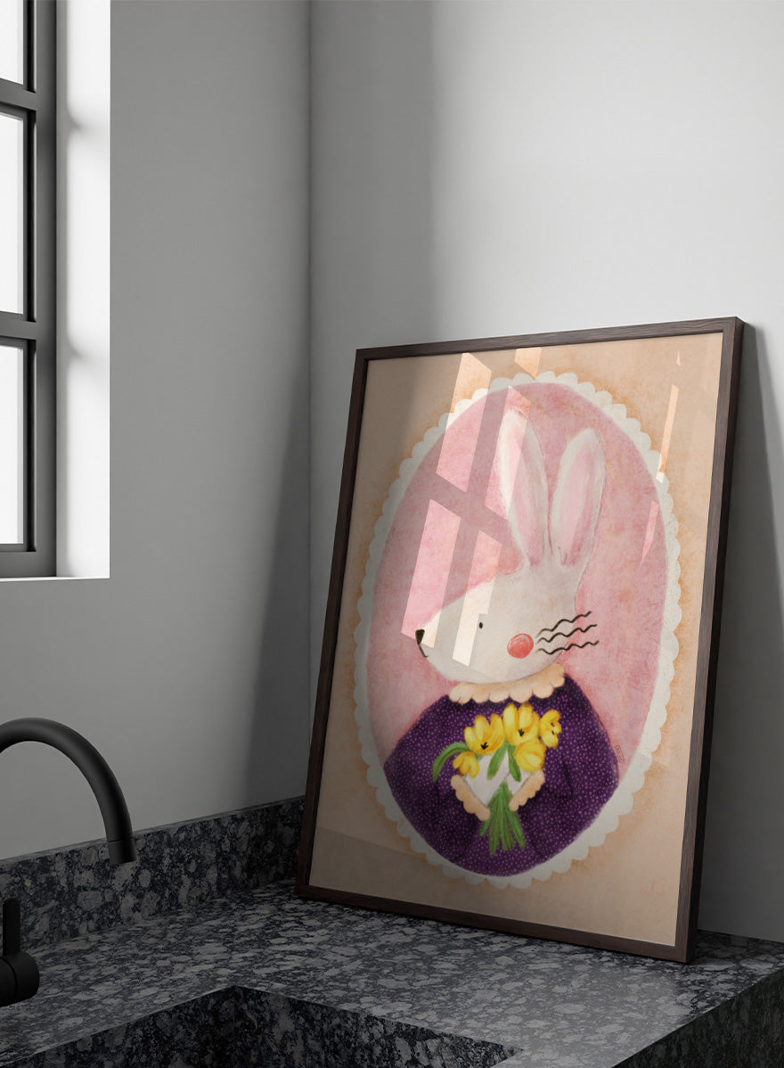 A framed art print featuring a whimsical illustration of a white rabbit in a purple dress holding yellow flowers, set against a pink oval background. Shop Charming Bunny With Tulips by Dirkie Nell, a playful animal portrait art print featuring a white bunny, yellow tulips, purple dress, and soft pink tones.