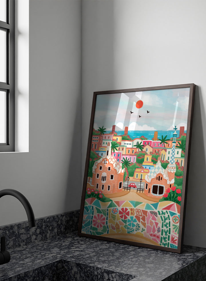 A colorful stylized illustration of a coastal town with pastel buildings, palm trees, a mosaic wall in the foreground, blue sea, and a red sun in the sky. Shop Colorful Coastal Dream by Nidhi Kachhadiya, a vibrant Barcelona wall art print inspired by Park Güell, Gaudí architecture, mosaics, and bright coastal color.