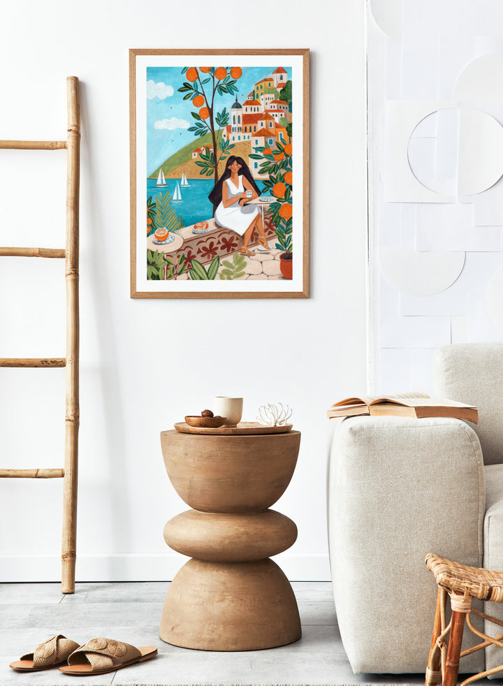Woman in a white dress sitting under an orange tree with a scenic coastal town in the background. Mediterranean Orange Grove View by Caroline Bonne Müller fine art print, wall art poster with coastal scene, orange trees, modern aesthetic design