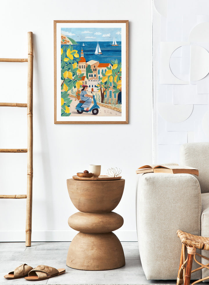 Illustration of a woman on a scooter with lemon trees and a coastal town in the background. Lemon Grove Scooter Ride by Caroline Bonne Müller summer coastal illustration art print with lemons, scooter and seaside town, colorful wall art poster