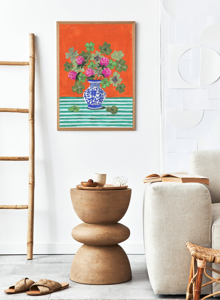 Vase with pink flowers and green leaves on a red and green striped background. Vibrant Clover Still Life by Caroline Bonne Müller is a fine art print and wall poster featuring clover leaves, pink flowers, and a blue vase on a striped table.