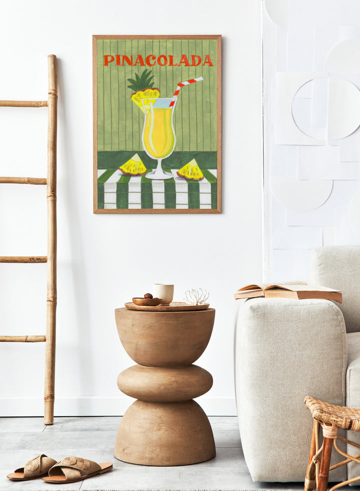 Illustration of a pina colada drink with pineapple slices on a checkered tablecloth. Piña Colada Summer Drink by Caroline Bonne Müller is a fine art print and wall poster of a pineapple cocktail with striped straw and green table setting.