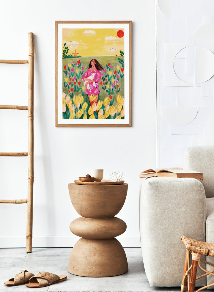 Woman holding a lamb in a field of flowers with a yellow sky and red sun. Woman Lamb Tulip Field by Caroline Bonne Müller is a fine art print and wall poster of a woman holding a lamb in a tulip field with a bright landscape.