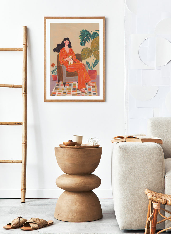 Illustration of a woman in an orange outfit sitting in a chair with plants around her. Cozy Home with Cat by Caroline Bonne Müller is a fine art print and wall poster featuring a woman in an orange outfit sitting with a cat in a warm, plant-filled interior.