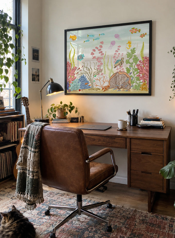 A framed art print depicting a colorful underwater scene with fish, coral, sea plants, a turtle, and a clam shell on a sandy ocean floor, shown against a light neutral background. Shop Vibrant Underwater World by Nikita Jariwala, an ocean wall art print poster with sea turtles, tropical fish, coral reef art, jellyfish, and blue tones.