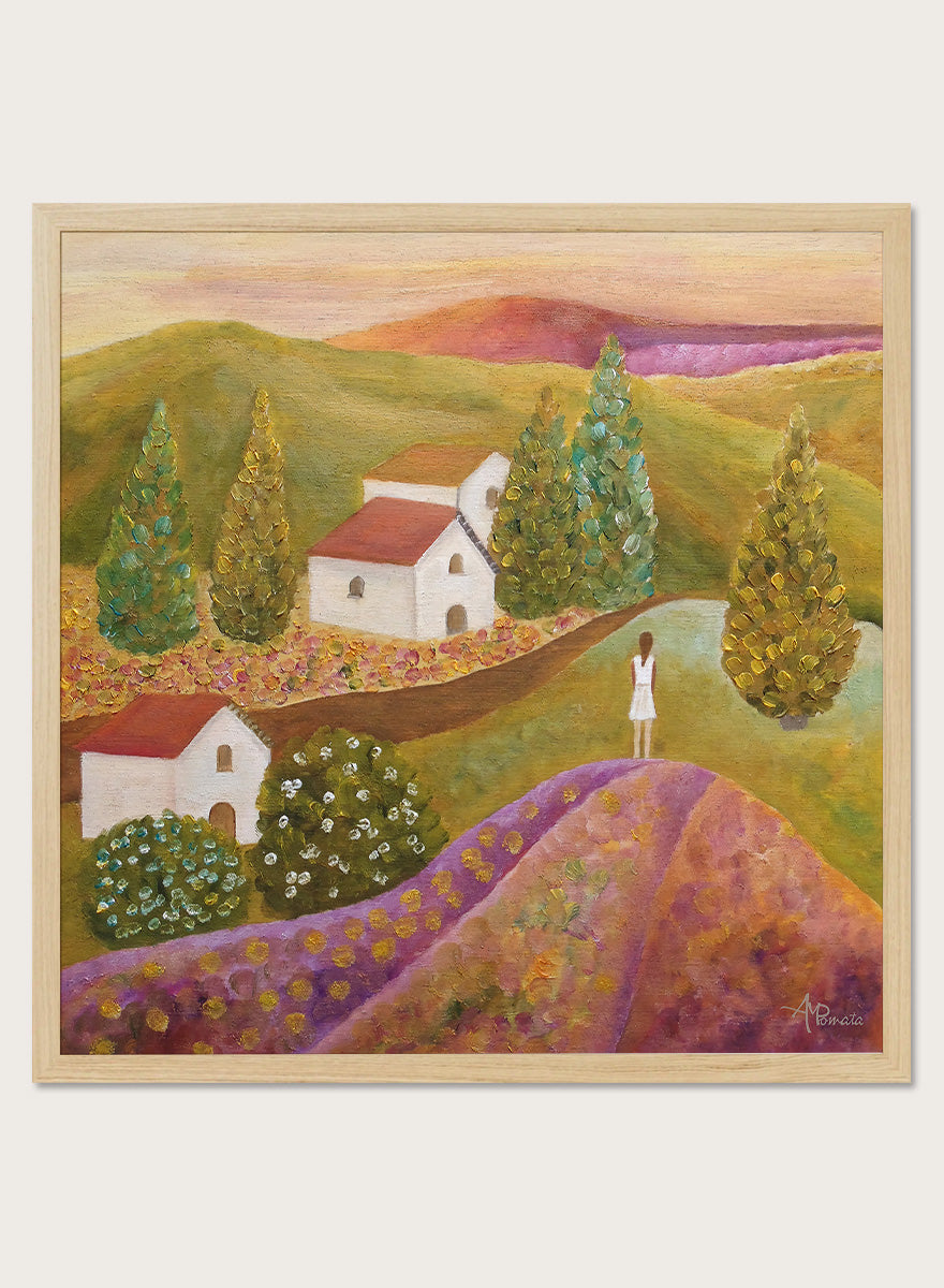A framed landscape painting featuring rolling green hills, white houses with red roofs, tall conical trees, and a figure standing on a purple field. Shop Woman in Lavender Fields by Angeles M. Pomata, a colorful landscape and figurative art print featuring lavender fields, white houses, cypress trees, and rolling hills.