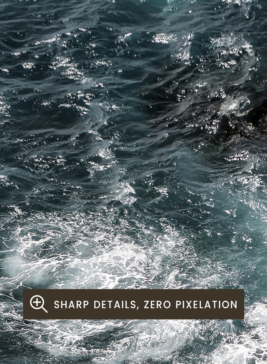 A framed photographic art print depicting a top-down view of turquoise ocean water washing over dark rocks and a rocky shoreline. Ocean’s Edge Symphony by Shot by Clint aerial ocean photography print featuring turquoise water, white surf, coastal texture, and soft seafoam tones.