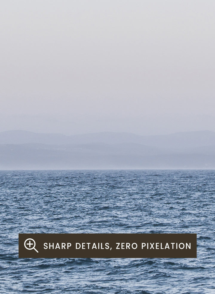 A minimalist framed art print depicting a calm blue ocean under a pale sky with a small visible moon. Moonlit Horizon by Shot by Clint coastal photography print featuring a pale moon, distant shoreline, open blue water, and soft lavender evening tones.