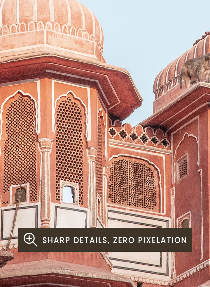 A framed art print featuring a photograph of the iconic pink sandstone Rajasthani palace, Udaipur, with white architectural details under a clear light blue sky. Terracotta Splendor by Shot by Clint architectural photography print featuring ornate palace windows, domed balconies, carved details, and warm coral tones.