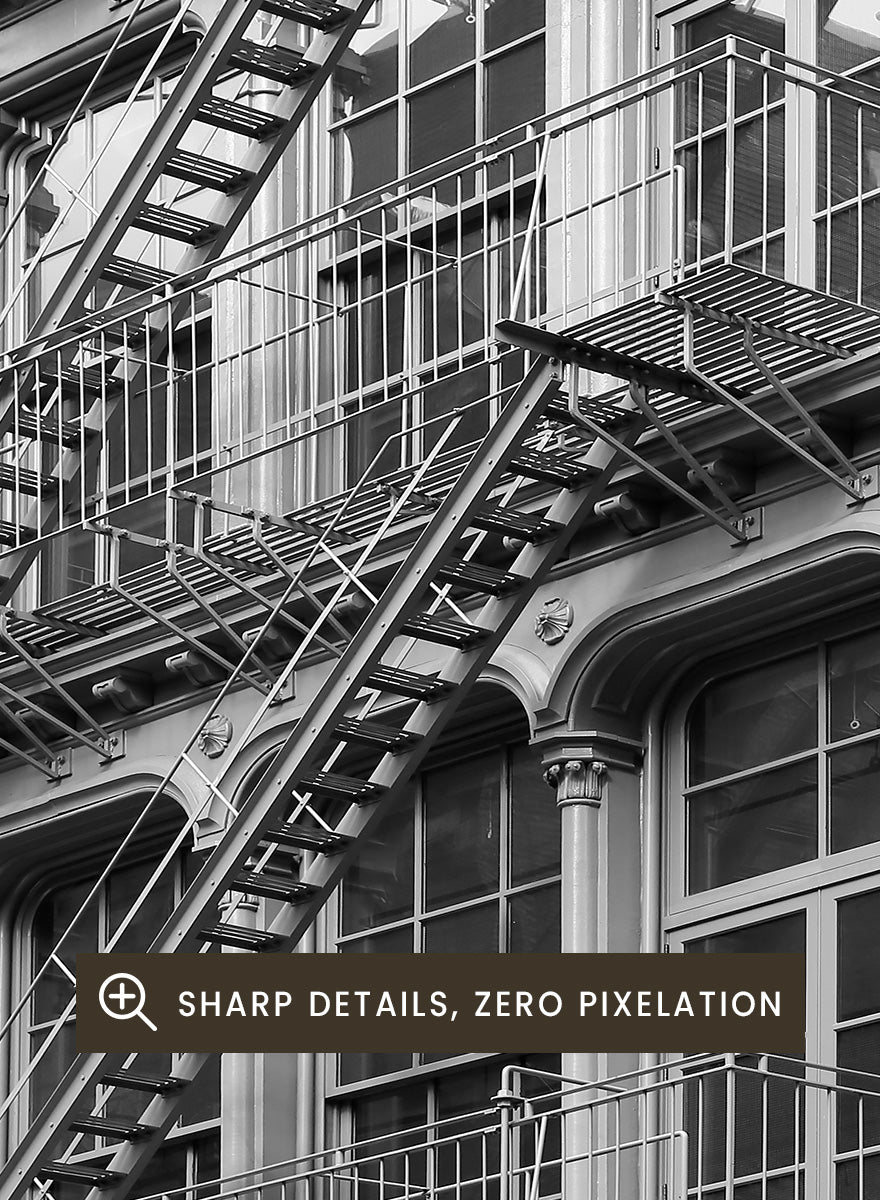Black and white architectural photograph of a corner building facade with ornate windows and external fire escapes. Urban Geometry by Shot by Clint black-and-white architectural photography print featuring fire escapes, tall windows, ornate columns, and layered city detail.
