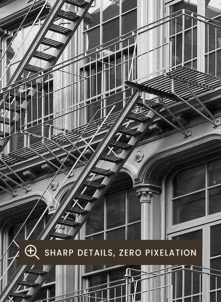 Black and white architectural photograph of a corner building facade with ornate windows and external fire escapes. Urban Geometry by Shot by Clint black-and-white architectural photography print featuring fire escapes, tall windows, ornate columns, and layered city detail.