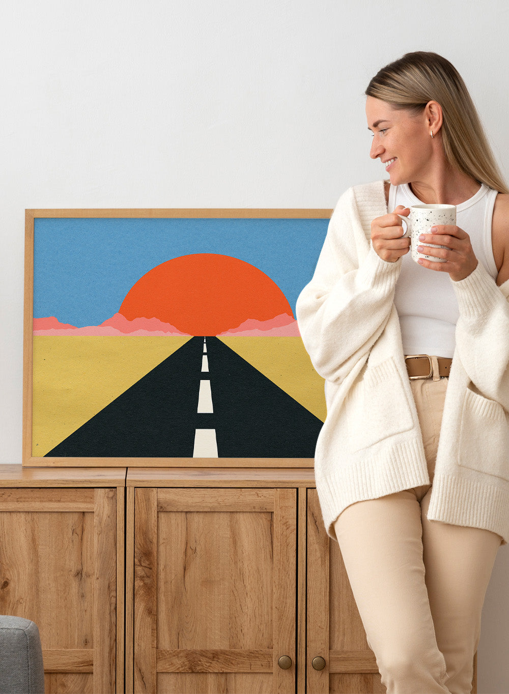 Simplified illustration of a road leading to a large red sun in a blue sky. Road To Sun by Rosi Feist is a modern landscape art print featuring a minimalist desert road, bold sunset colors, and contemporary graphic poster design.