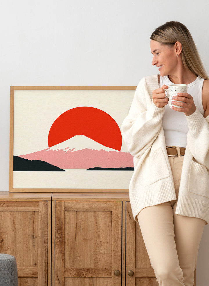 Framed artwork of a mountain with a red sun on a beige background. Fuji Sun by Rosi Feist is a modern Japanese landscape art print featuring Mount Fuji, a bold red sun, and minimalist contemporary poster design.