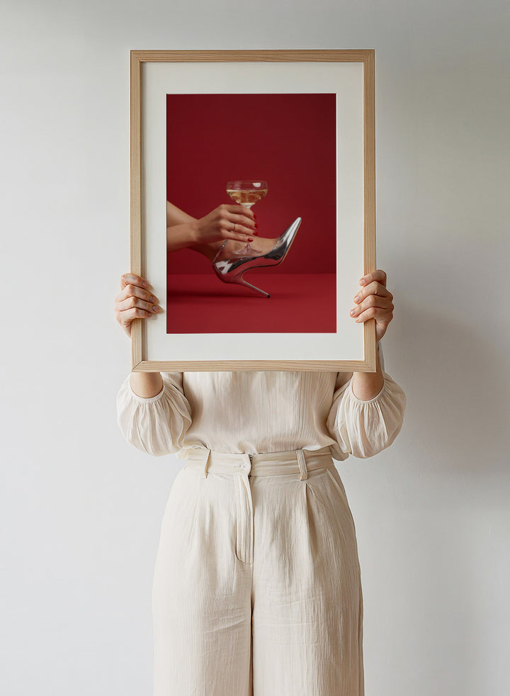 High-heeled shoe holding a glass of white wine against a red background, High Heels and Champagne by Andreas Magnusson is a fashion illustration art print featuring high heels, champagne glass imagery, bold red tones, and modern contemporary wall art style.