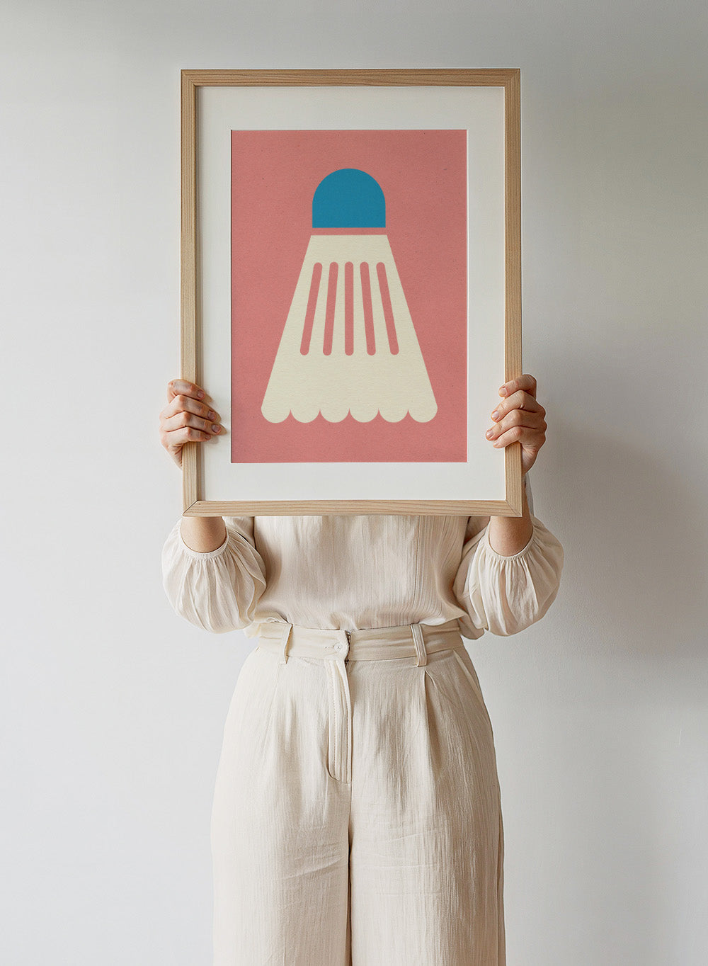 Shuttlecock with blue top and white body on a pink background. Badminton White Blue by Rosi Feist is a modern sports wall art print featuring a minimalist shuttlecock design in bold color and graphic poster style.