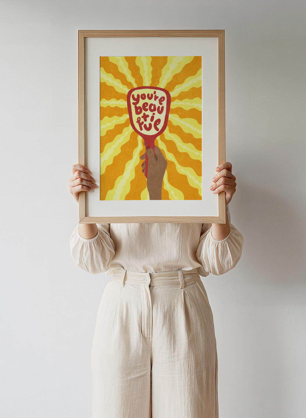Hand holding a sign with 'You're beautiful' on an orange and yellow background. Beautiful by Raissa Oltmanns is a modern motivational art print featuring a hand mirror illustration, bold lettering, and bright statement wall poster style.