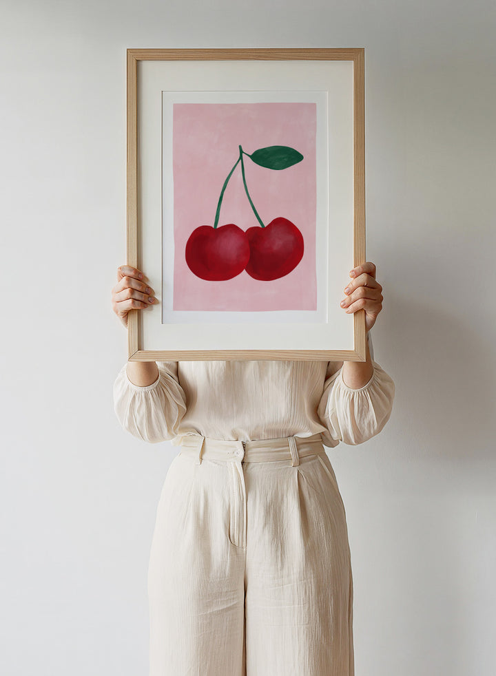 Two red cherries with a green stem on a pink background. Red cherries art print by Elena Ristova featuring two hand-painted cherries with green stems on a soft pink background. Officially licensed minimalist wall poster.
