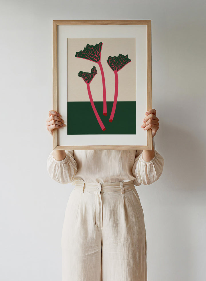 Illustration of red rhubarb stalks with green leaves on a beige and green background. Swedish Garden Rhubarb by Rosi Feist is a modern botanical art print with bold minimalist color and Bauhaus-inspired design. Officially licensed fine art poster with framing.