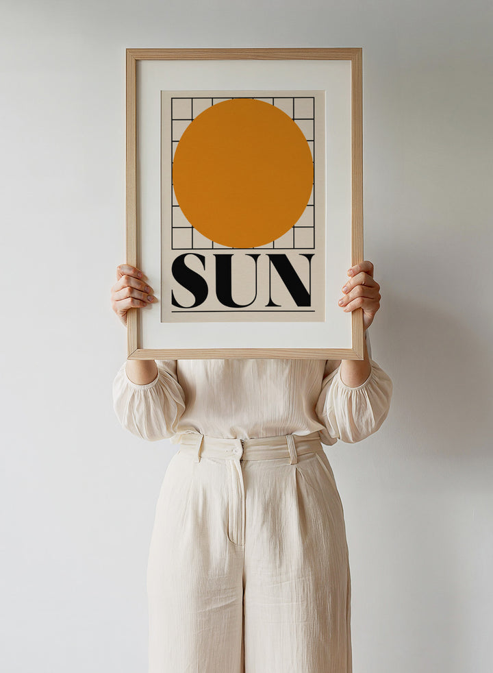Poster with a large orange circle and the word 'SUN' on a beige background. Sun by Rosi Feist is a bold minimalist Bauhaus-inspired art print featuring an orange circle and graphic grid. Officially licensed modern poster with framing.