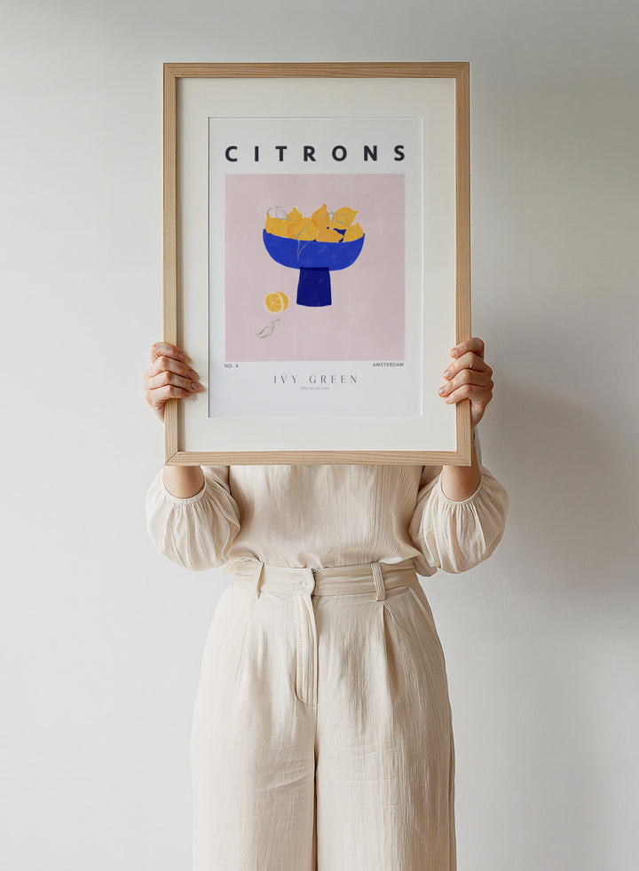 Illustration of lemons in a blue bowl on a pink background with 'Citrons' text and 'Ivy Green' branding. Citrons by Ivy Green lemon art print featuring bowl of lemons illustration, modern fruit poster design, and colorful contemporary kitchen wall art.