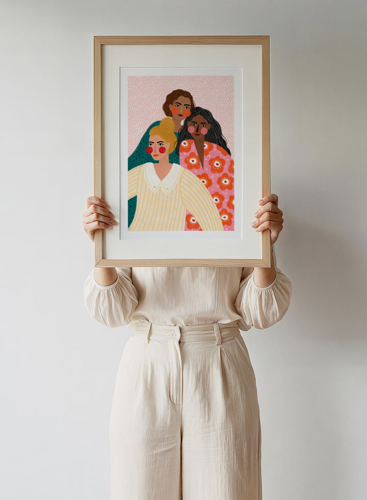 Illustration of three women with colorful clothing and patterns on a pink background. Girl Friends by Bea Müller is an officially licensed art print featuring three women illustrated in her signature bold colors and modern expressive style.