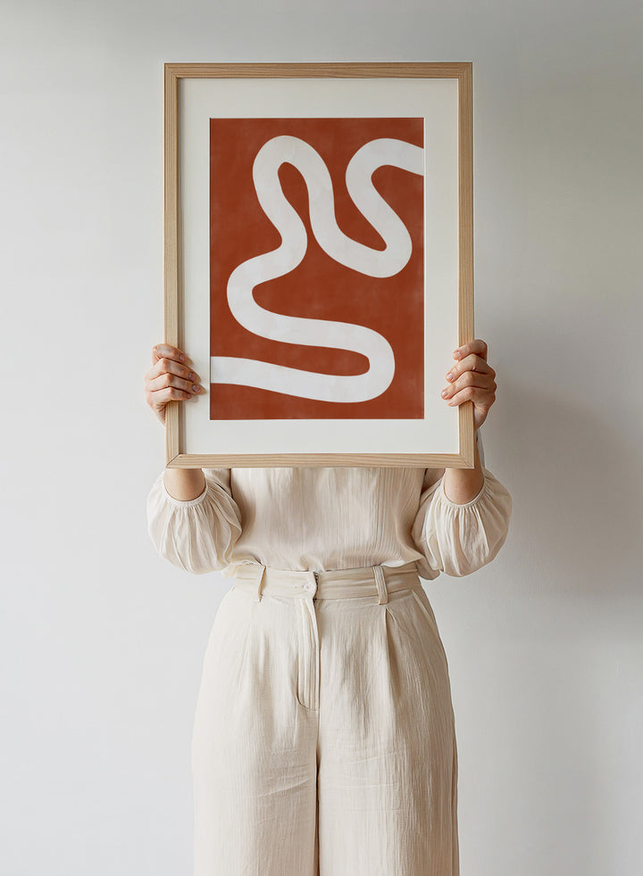 White wavy line on a red background. Crimson Pathways art print by Elena Ristova featuring a flowing white abstract line on a rust red background. Officially licensed modern abstract wall poster.
