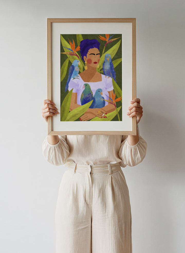 Artistic depiction of a woman with blue hair surrounded by parrots and tropical plants. Frida and Birds by Raissa Oltmanns is a modern Frida Kahlo inspired art print with tropical birds and bold botanical wall poster design.