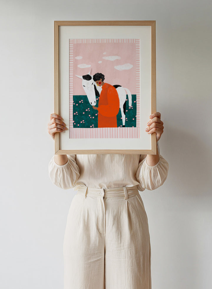 Illustration of a person in an orange outfit hugging a white horse against a pink background with clouds. Vibrant Girl and Horse by Bea Müller is a colorful girl and horse art print featuring modern expressive illustration. Officially licensed wall poster with optional framing.