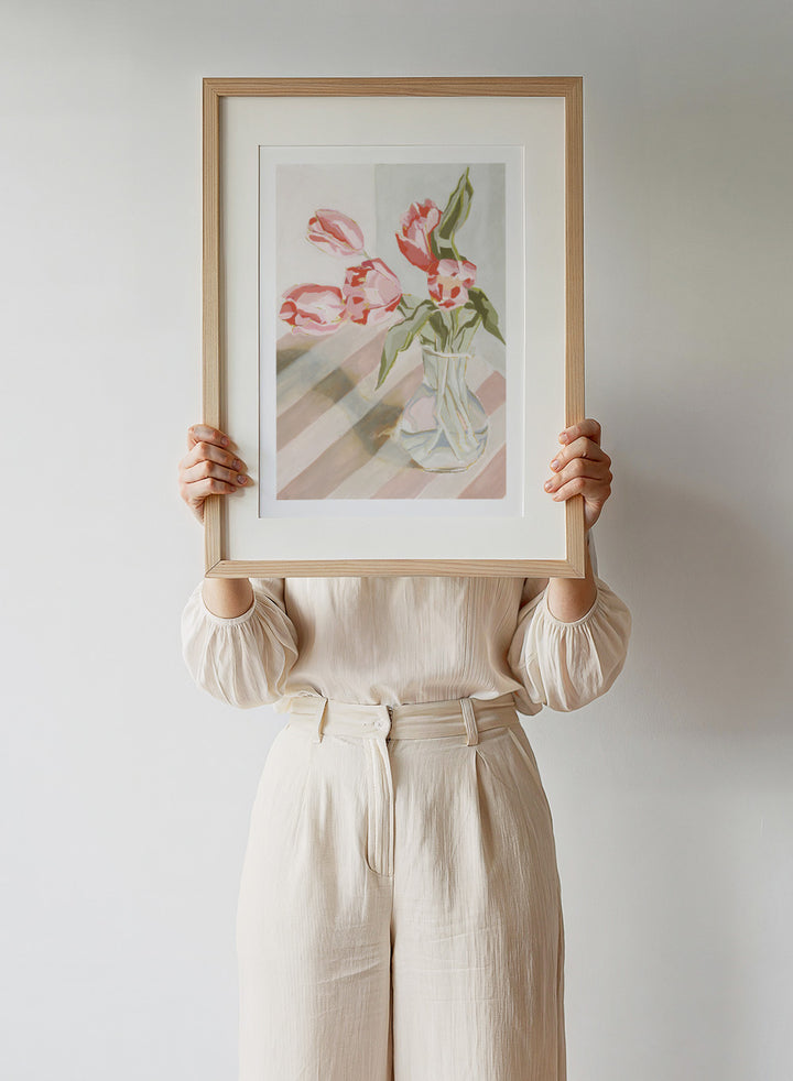 Artistic depiction of pink tulips in a clear vase on a striped background. Tulips in a Vase by Lucrecia Caporale is an officially licensed still life art print featuring pink tulips in a glass vase. Available framed or unframed.