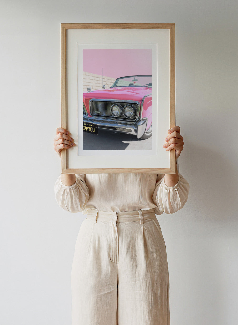 Pink vintage car with 'I ❤️ YOU' license plate against a pink sky. P.S. I Love You by Tom Windeknecht is officially licensed photography featuring a vibrant pop-art style photo of a car with romantic typography. Framed or unframed.