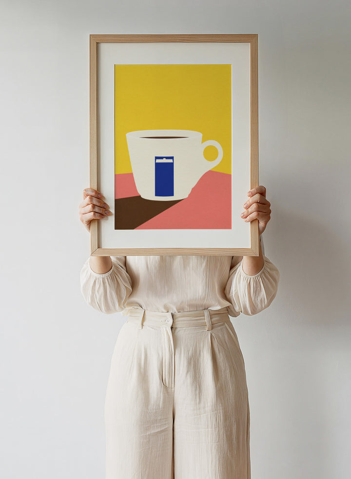 White coffee cup with a blue book design on a yellow and pink background. Tazza by Rosi Feist is a minimalist modern art print of a coffee cup in bold Bauhaus-inspired color blocks. Officially licensed fine art poster with framing.