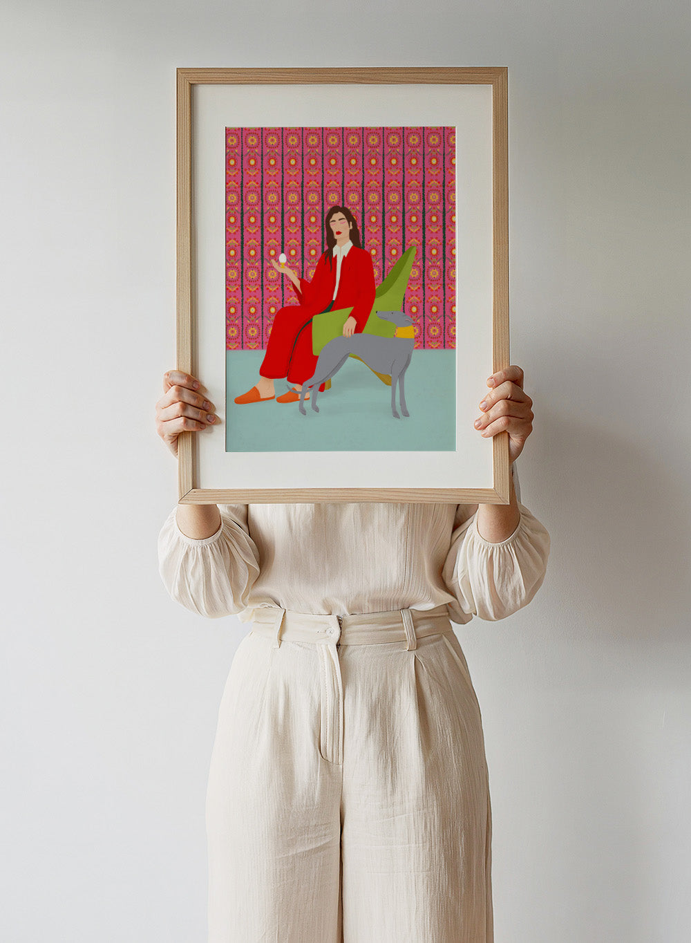 Woman in a red coat sitting on a green chair with a dog, against a pink patterned wall. Wonderful Egg by Jota de Jai is a whimsical modern art print of a woman in a red robe holding an egg with her greyhound, officially licensed wall poster with framing.