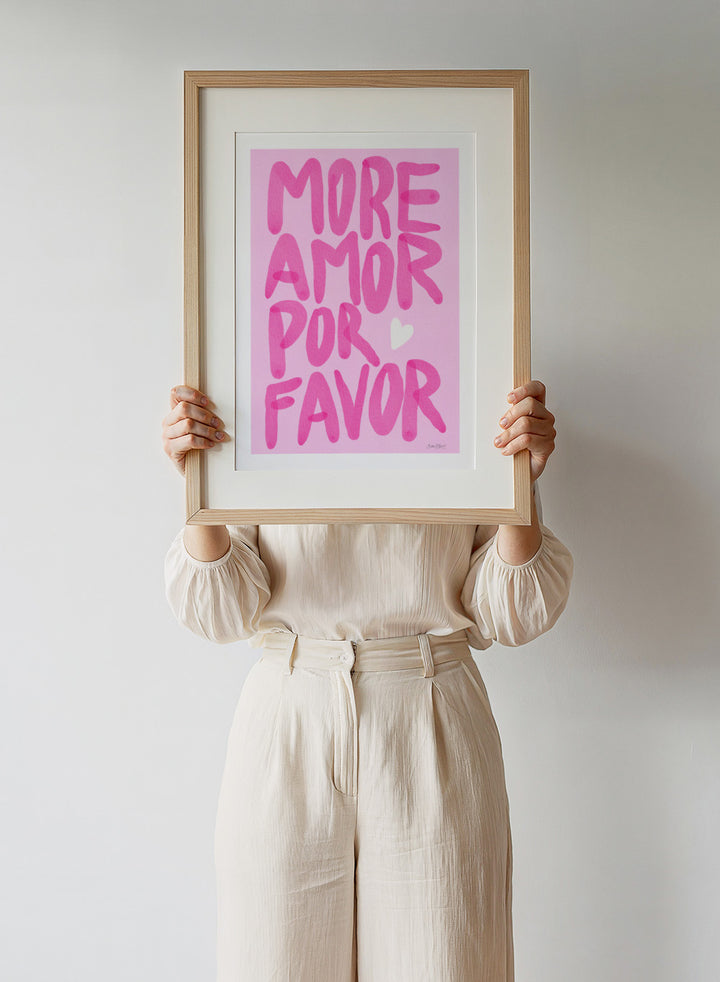 Pink text 'More Amor Por Favor' with a heart on a pink background. More Amor Por Favor by Baroo Bloom features bold pink hand-painted typography and a playful love message. Officially licensed wall poster with optional framing.