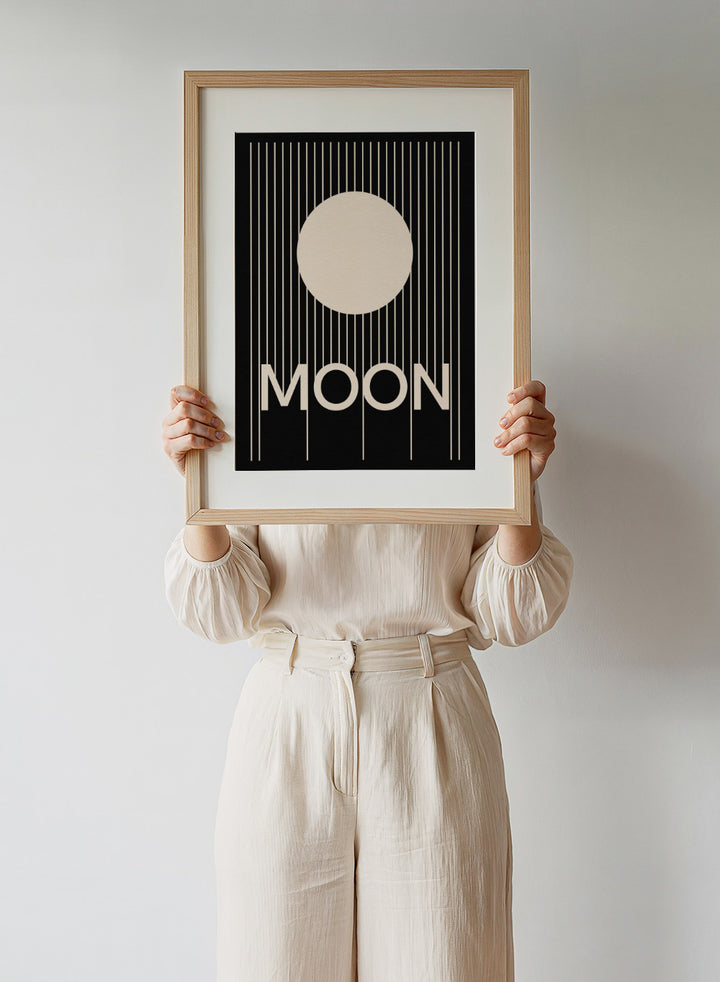 Poster with a stylized moon and the word 'MOON' on a black background. Moon by Rosi Feist is a bold minimalist Bauhaus-inspired art print with a cream circle and graphic lines. Officially licensed modern poster with framing.