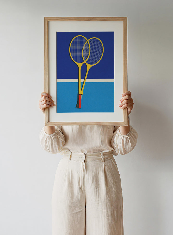 Two yellow badminton rackets on a blue background with a white stripe at the bottom. Wooden Badminton Rackets by Rosi Feist is a modern minimalist fine art print featuring bold yellow rackets on a graphic blue court. Officially licensed wall poster with optional artisan framing.