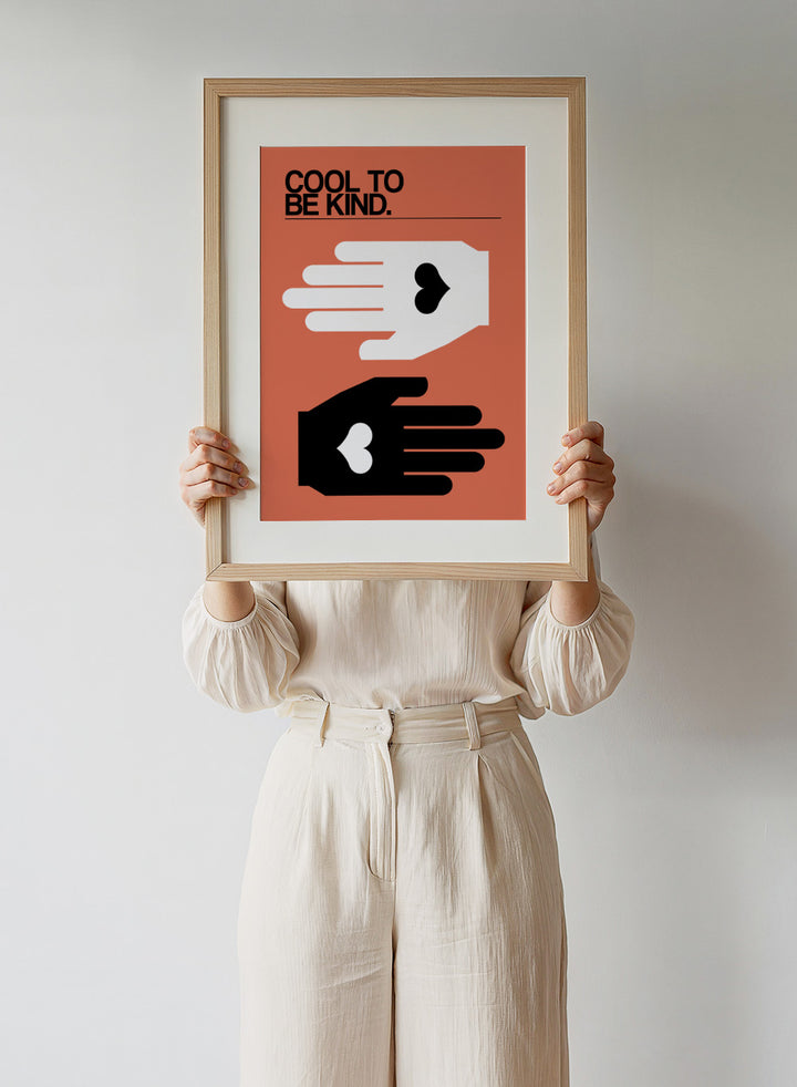 Poster with two hands reaching towards each other, one white and one black, on an orange background with 'Cool to be kind' text. Cool To Be Kind by Frances Collett is a modern kindness art print featuring two graphic hands with heart symbols. Officially licensed contemporary wall poster with optional framing.