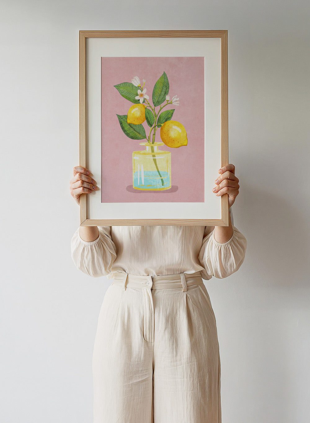 Illustration of lemons and a flower in a glass bottle on a pink background. Lemon Bunch In Vase by Raissa Oltmanns is a modern lemon still life art print featuring citrus fruit and floral kitchen wall poster design.