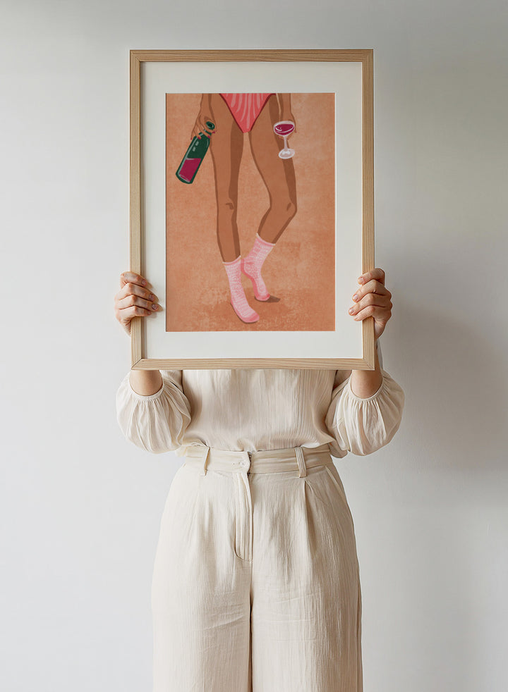 Illustration of a person's legs wearing pink socks with text, holding a bottle and a glass on a peach background. Wine and Socks by Raissa Oltmanns is a modern woman art print featuring wine bottle and glass in bold contemporary wall poster style.