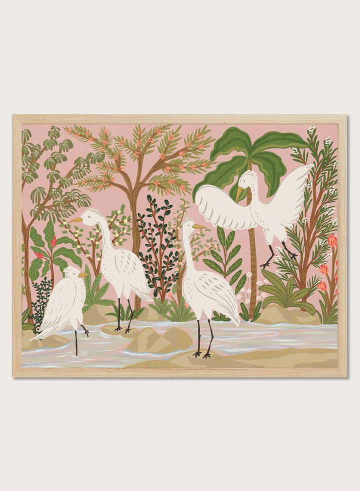 A framed art print featuring a stylized illustration of four white cranes in a tropical landscape with palm trees, green foliage, and a pink sky, displayed on a light beige wall. Shop Peaceful Jungle Egrets by Nikita Jariwala, a tropical bird wall art print featuring white egrets, lush greenery, botanical detail, and soft pink tones.a