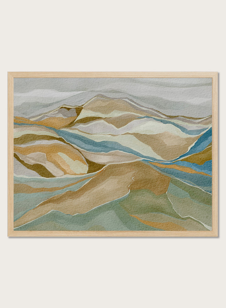 Framed abstract landscape wall art featuring layered hills and winding blue river-like lines in beige, tan, muted green, and blue tones, shown against a light neutral background. Shop Abstract Mountain Serenity by Nikita Jariwala, a modern mountain wall art print featuring layered abstract hills, earthy tones, and soft blue and sage accents.