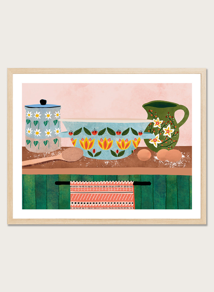 Framed art print featuring a whimsical still life illustration of kitchenware, including a floral-patterned bowl, a green pitcher, eggs, and a patterned towel. Charming Folk Kitchen by Ceyda Alasar kitchen art print featuring painted pottery, floral patterns, wooden spoons, eggs, and colorful folk-inspired decor.
