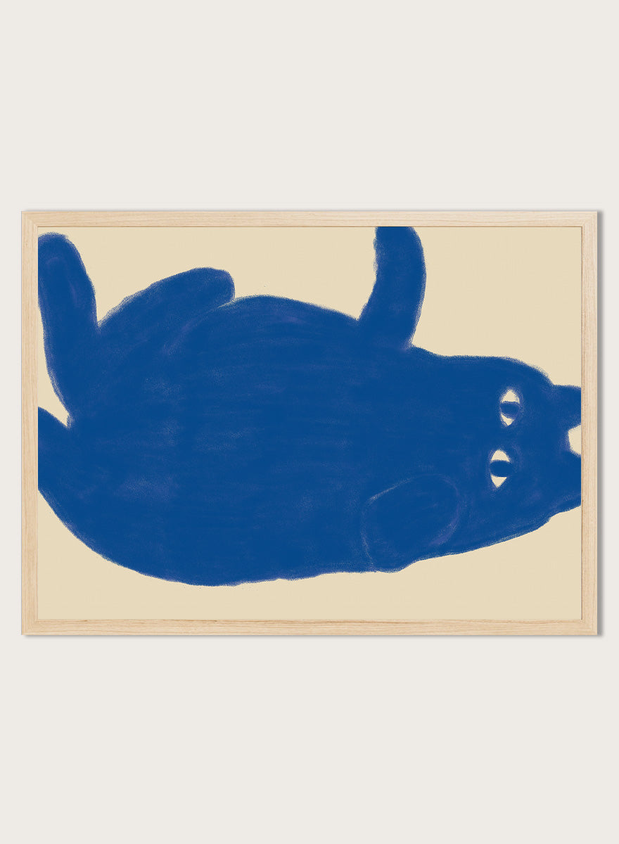A framed art print featuring a bold blue abstract cat illustration on a warm beige background. Whimsical Blue Cat by The Art Concept is a playful cat art print featuring a lounging blue cat on a warm cream background in a bold minimalist style.
