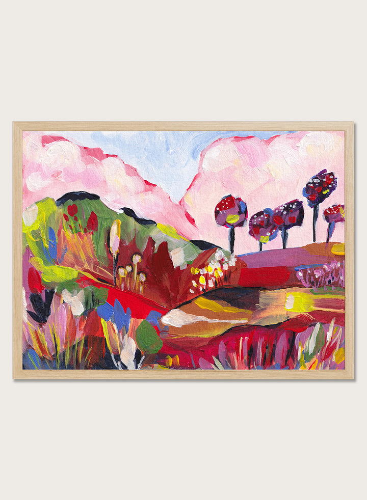 A framed abstract landscape painting featuring pink clouds, green hills, and colorful stylized trees. Shop Vibrant Fantasy Landscape by Dirkie Nell, a colorful landscape art print featuring pink clouds, rolling hills, wildflowers, and bold abstract color.